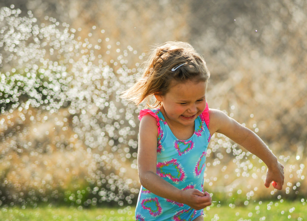 Child Playing in Sprinkler in Front Yard