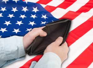Hands opening empty wallet in front of American flag. 