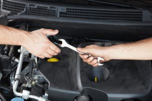  male hand offering wrench to hand of a friend under the hood of a car