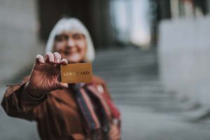 Older woman holding up credit card on bank steps