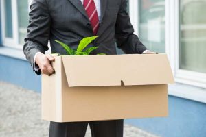  Man in business suit holding cardboard box with plant in it.