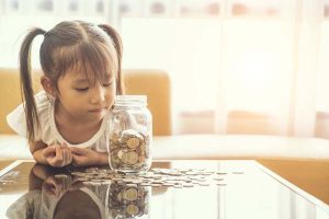 Little girl looking at clear glass jar filled with coins.