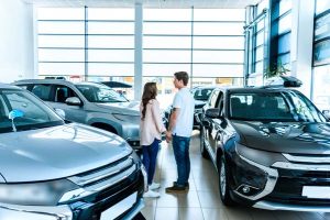 Man and woman holding hands standing in showroom of car dealership. 