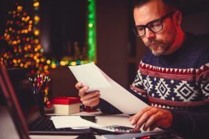 man at table concentrating on financial paperwork. Christmas decorations in background.