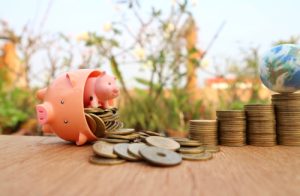 Turned over piggy bank with smaller piggy bank coming out with gold coins neatly stacked.