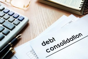 Desk with pens, calculator, glasses, notebook, and papers with the words “Debt Consolidation”