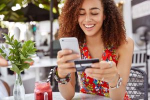 Young woman looking at smartphone holding credit card as to enter payment information for online shopping