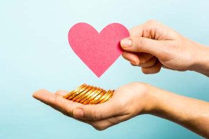 Hands holding a paper heart and gold-colored coins